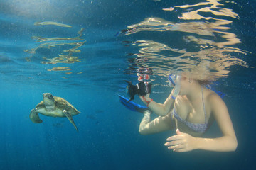Sea Turtle and young woman snorkeling and photographing it