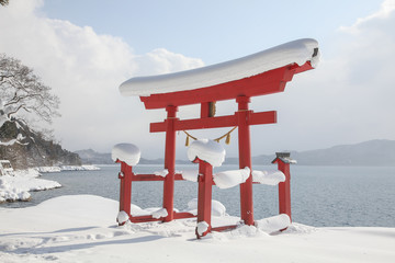 A red Torii gate of Japanese shrine and Lake Tazawa in snow