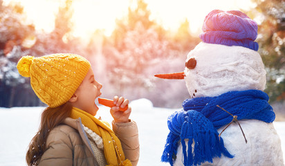 happy child girl plaing with a snowman on a snowy winter walk