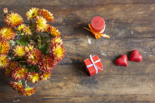 Valentine's Day gift, red chocolate hearts, candle and golden chrysanthemum on wooden background