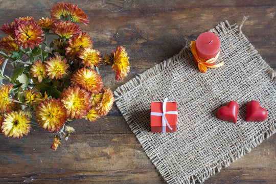 Valentine's Day gift, red chocolate hearts, candle and golden chrysanthemum on wooden background