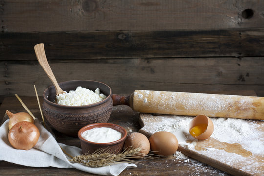 Rustic natural dairy products. Rustic natural dairy products cottage cheese, sour cream in clay dishes, eggs and ears of wheat on the old wooden background.