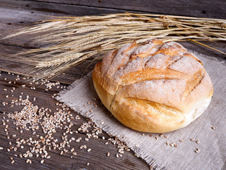 Homemade bread and ripe ears of wheat on a wooden background