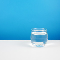 The small round glass of pure water on a white table.