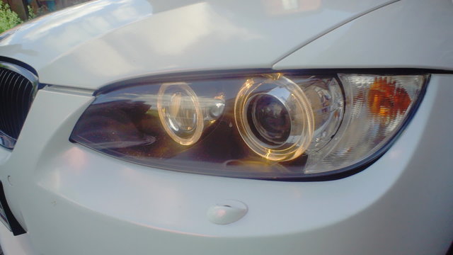 The light of the white car headlight turns on. Close up