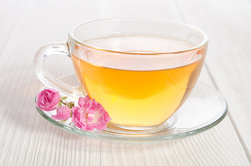 Glass cup of tea with  rose on white wooden table