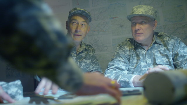  Military officers in army bunker, looking at map & discussing battle strategy