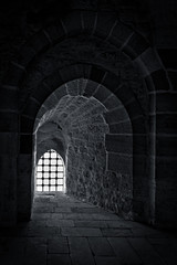 Fototapeta premium Stone wall with one backlit window with iron grid at one of the passages of an old citadel, Alexandria, Egypt. A fifteenth century defensive fortress located on the Mediterranean sea coast