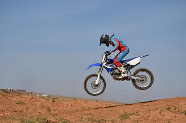 Motorcycle racer completes a jump, standing on a motorcycle motocross tilted forward