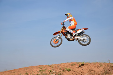 Motocross athlete individually in air flying over the hill land, against the blue sky