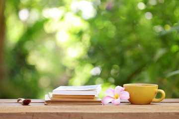 yellow coffee cup with flower and notebook on wooden table