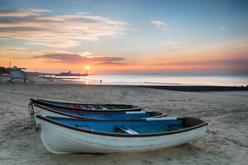 Photo sur Plexiglas Jetée Stunning sunrise ove rfishing boats at Durley Chine on Bournemouth beach in Dorset with the sun rising over the end of the pier