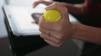 Hispanic young woman typing on tablet pc in modern executive office of corporate building. She plays with antistress ball. Closeup shot
