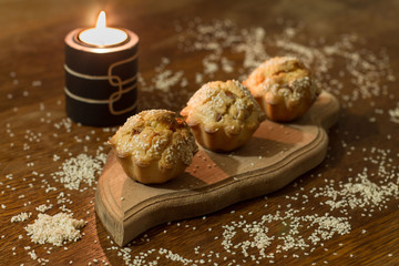 Three salty muffins with sausage, cheese and sesame on wood cut boarding near candle.