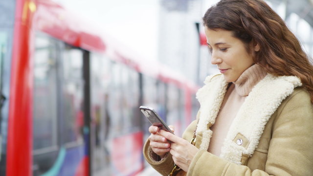  Young attractive woman texting on smartphone as train comes into station