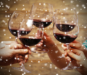 Clinking glasses of red wine in hands on wooden background over snow effect