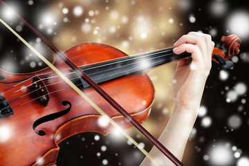 Beautiful young girl with classical violin on bright background over snow effect
