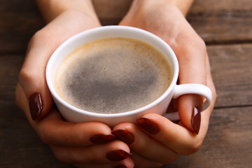 Female hands holding cup of coffee on wooden background