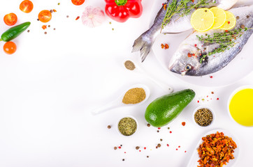 Fresh raw gilthead fishes with lemon, herbs, olive oil, avocado, paprika, ?herry tomatoes, garlic, salt on white background. Healthy food concept. Food frame