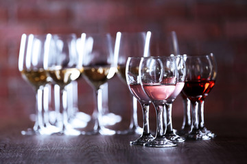 Wineglasses with white, red and pink wine on wooden table on wall brick background