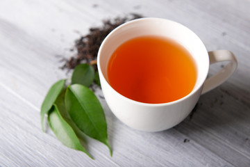Ceramic cup of tea with scattered tea leaves around on light wooden background
