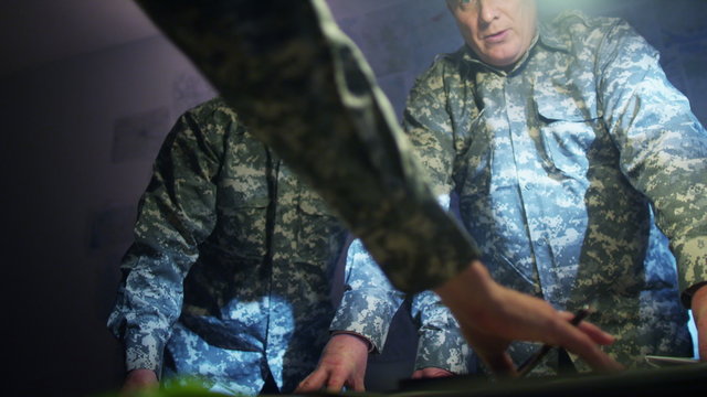  Military officers in army bunker, looking at map & discussing battle strategy