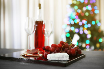 Fototapeta na wymiar Pink wine bottle, two wineglasses, grape, slices of bacon and cheese on Christmas background