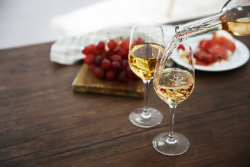 Pouring white wine from bottle into the wineglass on the table