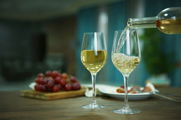 Pouring white wine from bottle into the wineglass on the table over blurred background