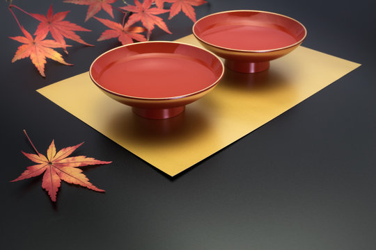vermilion lacquer coated sake cup and maple leaves on the black background. in Japan, vermilion sake cups are used for festive meals, especially for New Year celebration or wedding ceremony.