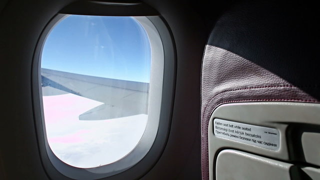 Airplane Window Seat - View of Wing of Plane on Flight, Traveling in Air over City and clouds