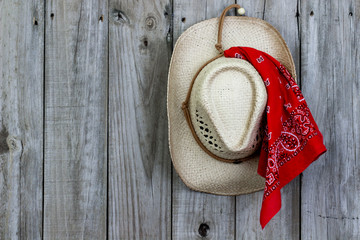 Cowboy hat with bandanna hanging on rustic background