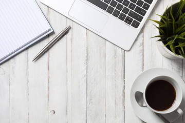 Notepad, laptop and coffee cup on wood table. View from above