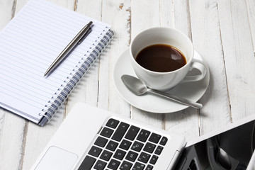 Notepad with pen, laptop and coffee on wooden table