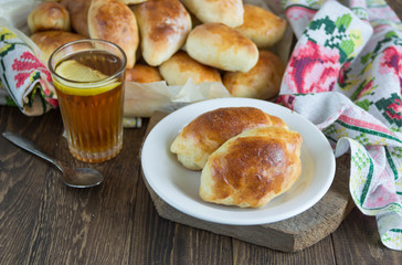 Russian pirozhki (baked patties) on wooden cutboard and lemon tea