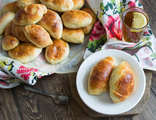 Russian pirozhki (baked patties) on wooden cutboard and lemon tea
