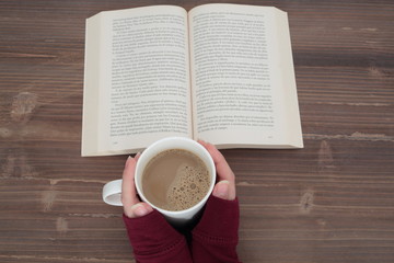 open book on wooden table and in the hands of a girl with a cup of coffee