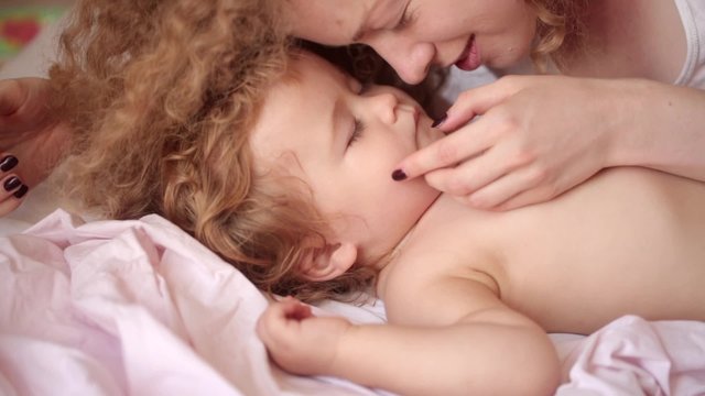 Newborn sleeping and enjoying the love of her curly young mother