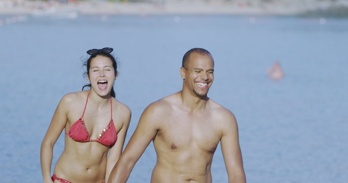  Happy attractive couple holding hands as they walk along the beach. Shot on RED Epic.