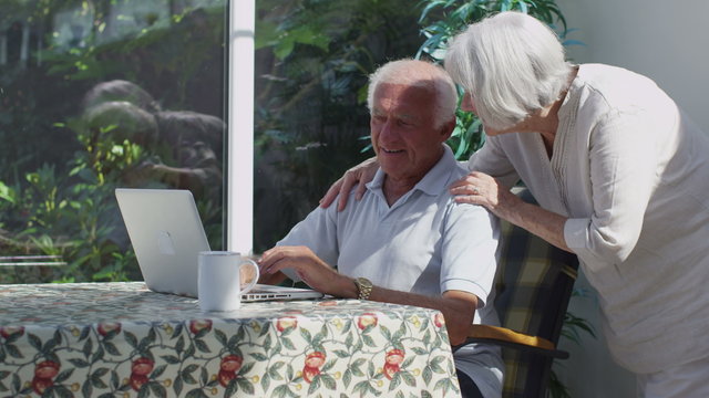 Cheerful senior couple relaxing in the conservatory with laptop computer