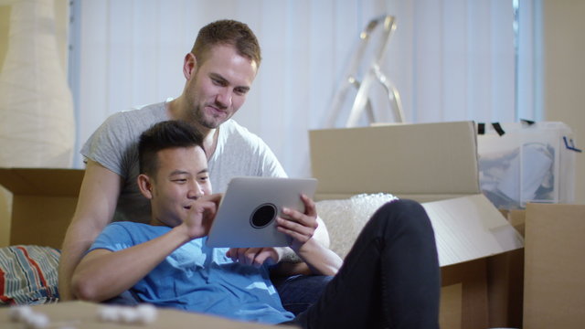  Happy young gay couple with computer tablet, moving into new home