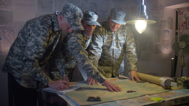  Military officers in army bunker, looking at map & discussing battle strategy