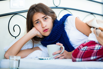 Sick teenage girl with hot tea and medication indoors