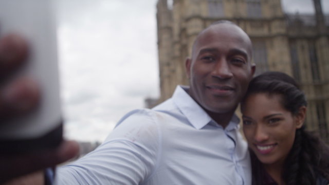  Happy attractive couple sightseeing in London taking a selfie in front of houses of parliament.