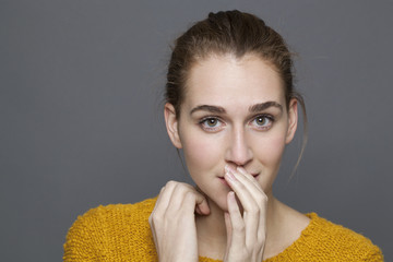 glowing happiness concept - confused 20s girl thinking with shy hand gesture for discretion and...