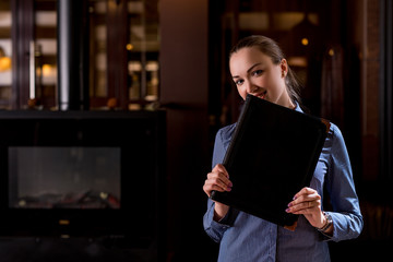 Smiling waitress hiding her face behind menu