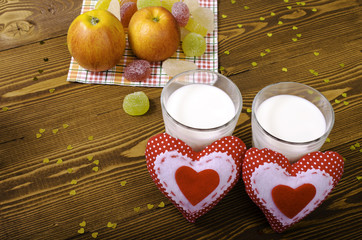 Two hearts, apples on a napkin and two glasses of milk.