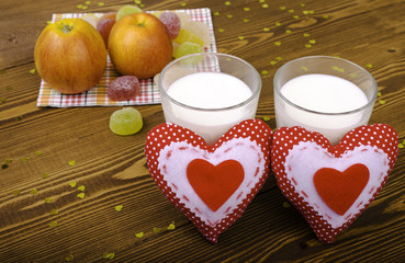 Two hearts, apples on a napkin and two glasses of milk.