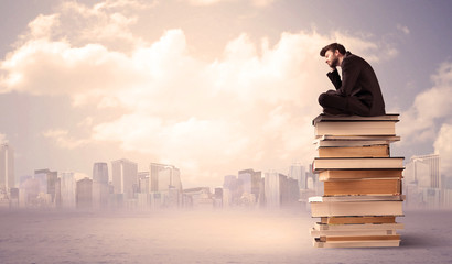 Man sitting on pile of books above city