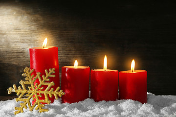 Burning candles and snowflake with snow on wooden background